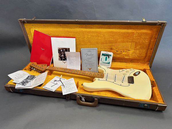 Vintage cream Fender Stratocaster electric guitar with maple neck and fingerboard, displayed in open vintage brown guitar case with yellow interior lining and assorted Fender manuals and paperwork