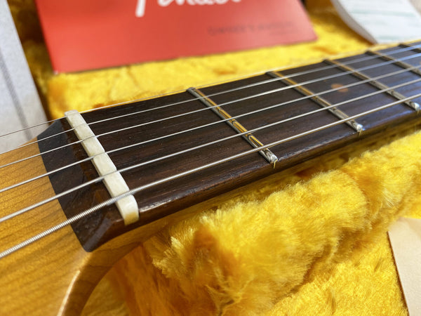 Close-up of acoustic guitar nut and strings on dark wood fingerboard in yellow plush case with red Fender booklet background