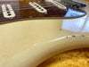 Close-up of vintage cream electric guitar body showing worn and chipped finish with visible cracks and tortoiseshell pickguard detail under guitar strings.