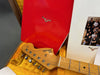 Close-up of Fender Stratocaster guitar headstock inside vintage yellow plush-lined hard case with red Custom Shop papers and photo insert