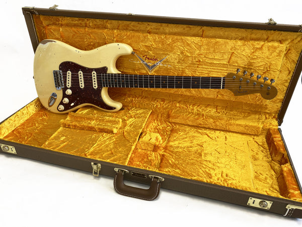 Vintage Fender Stratocaster electric guitar in worn white finish with tortoiseshell pickguard, resting in open yellow velvet lined Fender hard case