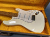 White electric guitar with maple fretboard and three single coil pickups in open guitar case with yellow plush interior