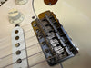 Close-up view of vintage Fender electric guitar bridge and volume knob with white pickguard and string saddles
