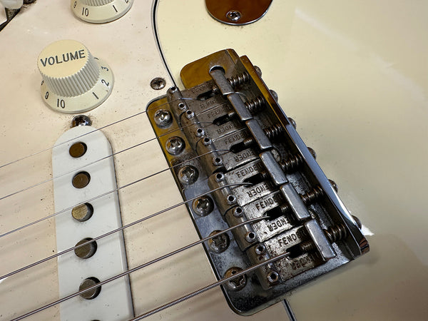 Close-up view of vintage Fender electric guitar bridge and volume knob with white pickguard and string saddles