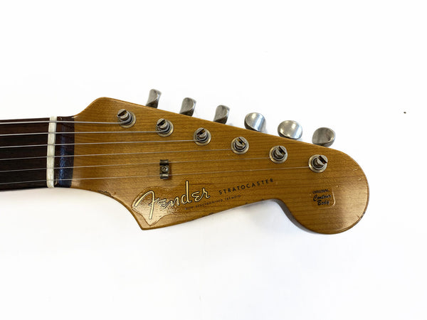Close-up of a vintage Fender Stratocaster guitar headstock showing tuning pegs, rosewood fretboard, and original contour body decal on natural wood finish.