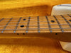 Close-up of maple guitar neck with metal frets and black dot inlays on an electric guitar in a yellow plush case interior