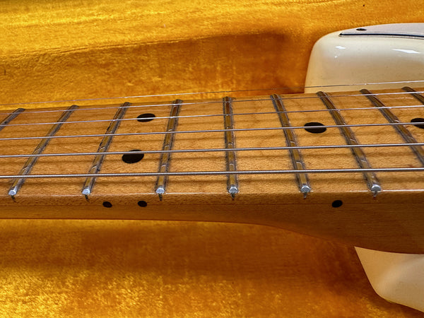 Close-up of maple guitar neck with metal frets and black dot inlays on an electric guitar in a yellow plush case interior