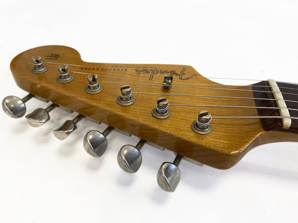 Close-up of vintage Fender Stratocaster guitar headstock with tuning pegs and strings on white background