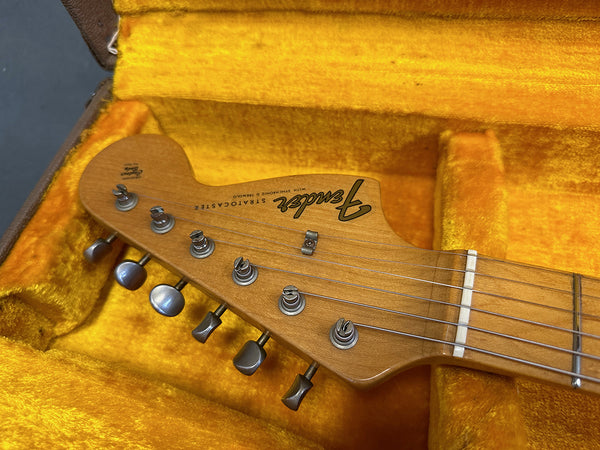 Close-up of Fender Stratocaster guitar headstock with six tuning pegs, natural wood finish, and strings, resting in yellow plush guitar case interior
