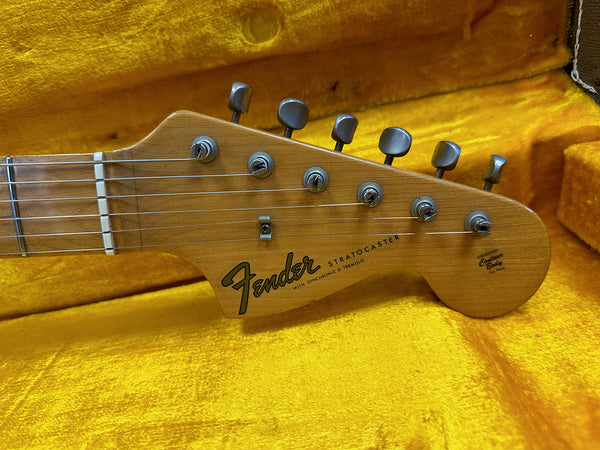 Close-up of Fender Stratocaster headstock with tuning pegs and strings on yellow plush guitar case lining