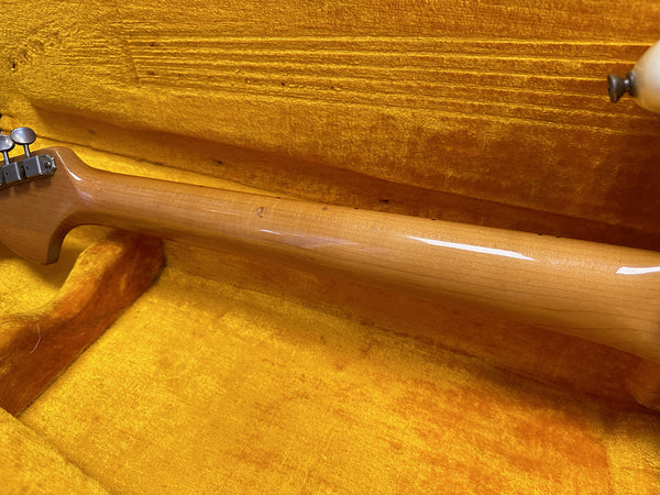 Glossy maple guitar neck with vintage tuner pegs resting in orange plush guitar case interior