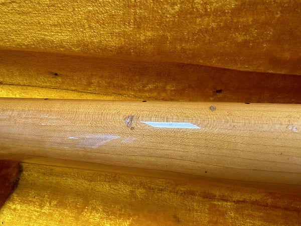 Close-up of a guitar neck showing wood grain and light wear inside a yellow plush case interior.