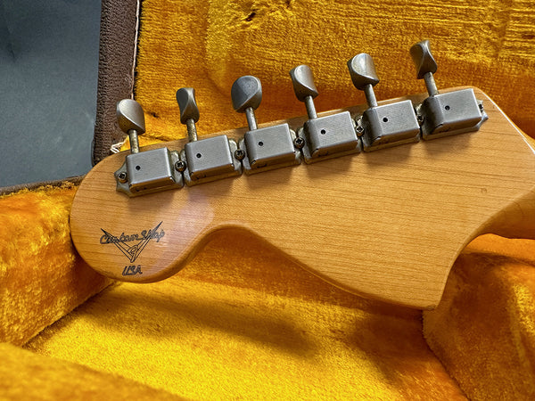 Vintage guitar headstock with six tuning pegs and Custom Shop USA logo, resting in a yellow plush guitar case interior