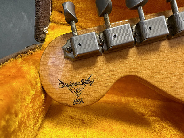 Close-up of vintage Fender Custom Shop guitar headstock with metal tuning pegs inside plush orange guitar case