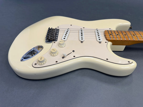 Cream colored electric guitar with maple neck and three single-coil pickups on gray background