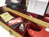 Fender Stratocaster electric guitar in candy apple red with maple neck and fretboard, displayed inside tweed hard case with red plush interior, including Fender paperwork, instruction manuals, custom shop tag, cable, and chrome neck plate.