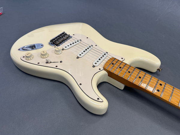 Close-up of vintage cream electric guitar body with maple fretboard, three single-coil pickups, and tone and volume control knobs on gray background