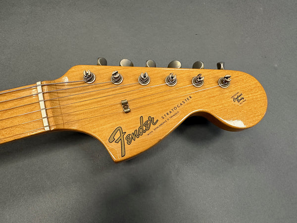 Close-up of natural wood Fender Stratocaster guitar headstock with tuning pegs and strings on gray background