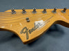 Close-up of natural wood Fender Stratocaster guitar headstock with six tuning pegs and strings on dark gray background