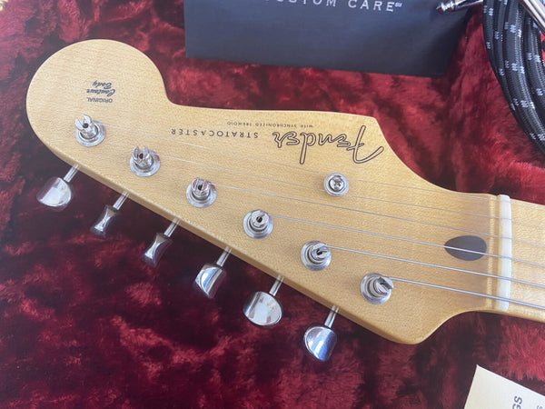 Close-up of Fender Stratocaster guitar headstock with tuning pegs on red plush background