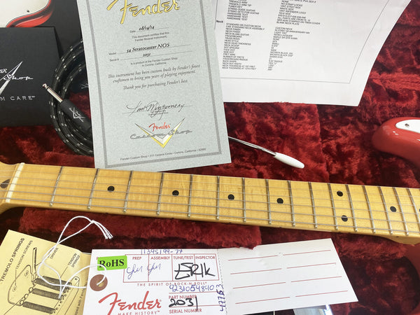 Fender Custom Shop certificate and specification sheet for 54 Stratocaster NOS guitar displayed on red plush guitar case lining with guitar neck, tremolo arm, and accessory tags.