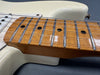Close up of maple guitar neck and fretboard with chrome frets and strings on cream electric guitar body