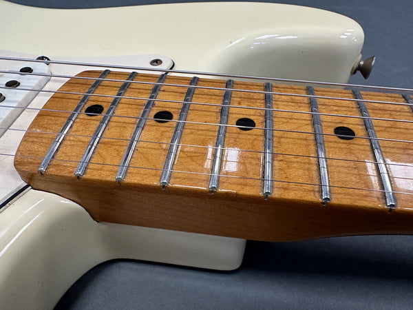 Close up of maple guitar neck and fretboard with chrome frets and strings on cream electric guitar body