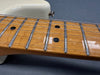 Close-up of maple guitar neck and fretboard with metal frets and black dot inlays on electric guitar with white body background