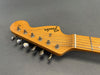 Close-up of Fender Stratocaster natural wood guitar headstock with six tuning pegs and strings on gray background