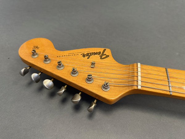 Close-up of Fender Stratocaster natural wood guitar headstock with six tuning pegs and strings on gray background