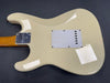 Back view of cream electric guitar body with white plastic backplate and maple neck with metal neck plate against dark background