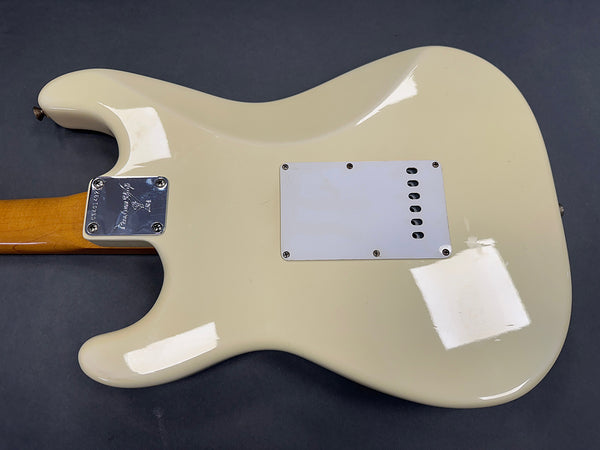 Back view of cream electric guitar body with white plastic backplate and maple neck with metal neck plate against dark background