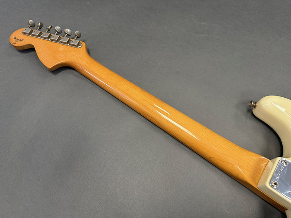 Close-up of vintage maple guitar neck and headstock with six tuning pegs on a gray background, showing smooth wood grain and part of an off-white guitar body.