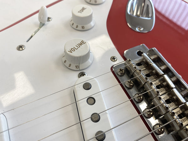 Close-up of white electric guitar volume and tone control knobs, pickup, metal bridge, and red body panel at Coffee House Guitars.