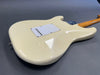 Back view of cream-colored electric guitar body with white backplate and maple neck on gray background