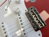 Close-up of red electric guitar bridge, white pickups, and volume control knob with "Volume" labeled on guitar body
