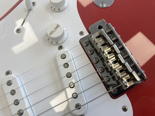 Close-up of red electric guitar bridge, white pickups, and volume control knob with "Volume" labeled on guitar body