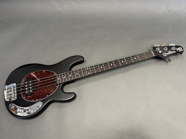 Black Ernie Ball Music Man StingRay bass guitar with tortoiseshell pickguard and chrome hardware on gray background
