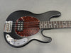Black electric bass guitar with tortoiseshell pickguard and chrome control knobs on gray background