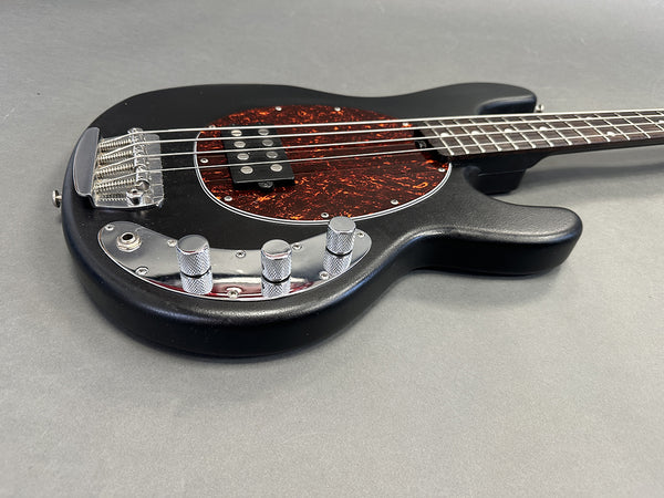 Black electric bass guitar with tortoise shell pickguard and chrome knobs on gray background