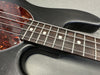 Close-up of guitar fretboard with metal frets and white dot inlays, black textured guitar body, and tortoiseshell pickguard with metal screws.