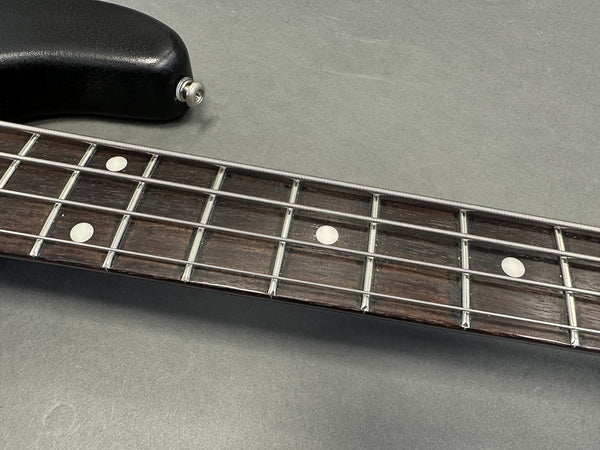 Close-up of bass guitar fretboard with metal frets, dot inlays, and four strings on gray background