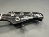 Close-up of black Music Man Sub Bass guitar headstock with tuning pegs and worn edges on gray background