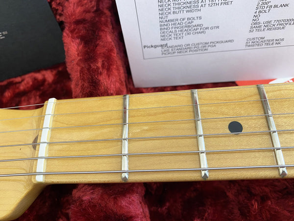 Close-up of maple guitar neck and fretboard with metal frets and black dot inlay, resting on plush red case lining with specification sheet in background