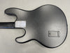 Black electric guitar back body with textured finish and neck plate screws visible, showing battery compartment door on gray surface