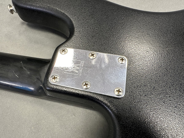 Close-up of black electric guitar neck joint with metal neck plate and screws on textured guitar body