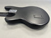Back view of black electric guitar body with textured finish and battery compartment cover on gray background