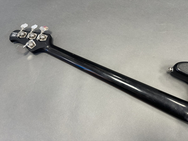 Black guitar neck with four silver tuning pegs on a gray background, Music Man bass guitar headstock view