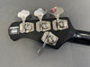 Close-up of black Music Man bass guitar headstock with four silver tuning pegs and Ernie Ball brand label made in San Luis Obispo, California USA