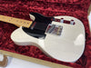 White electric guitar with black pickguard and maple neck resting in red plush-lined guitar case